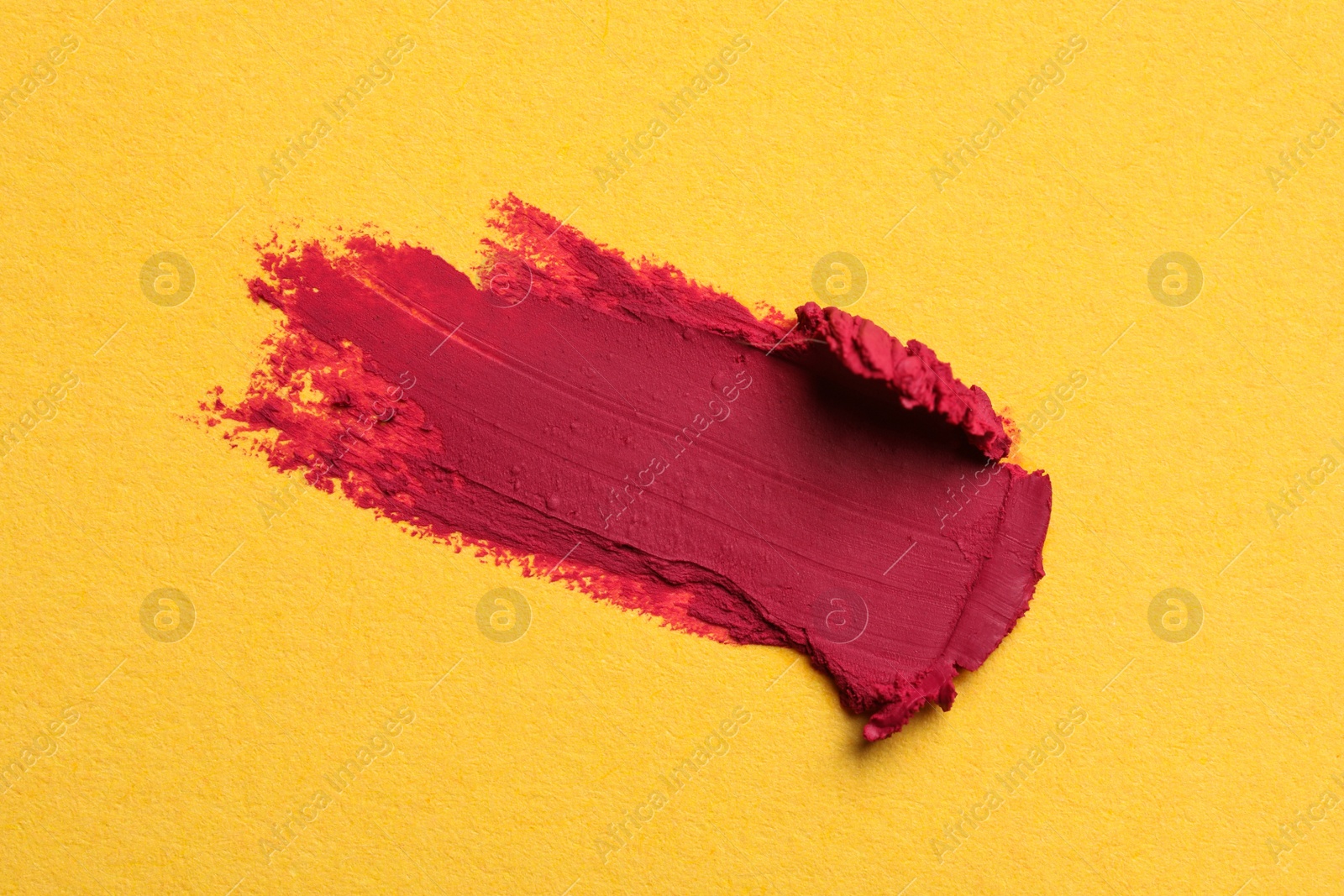 Photo of Smear of bright lipstick on yellow background, top view