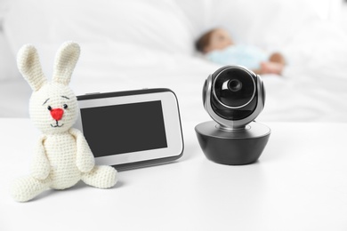 Photo of Baby monitor, camera and toy on table near bed with child in room. Video nanny