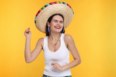 Photo of Young woman in Mexican sombrero hat dancing on yellow background