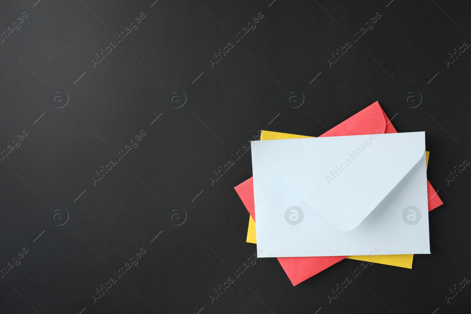Photo of Stack of colorful paper envelopes on black background, top view. Space for text