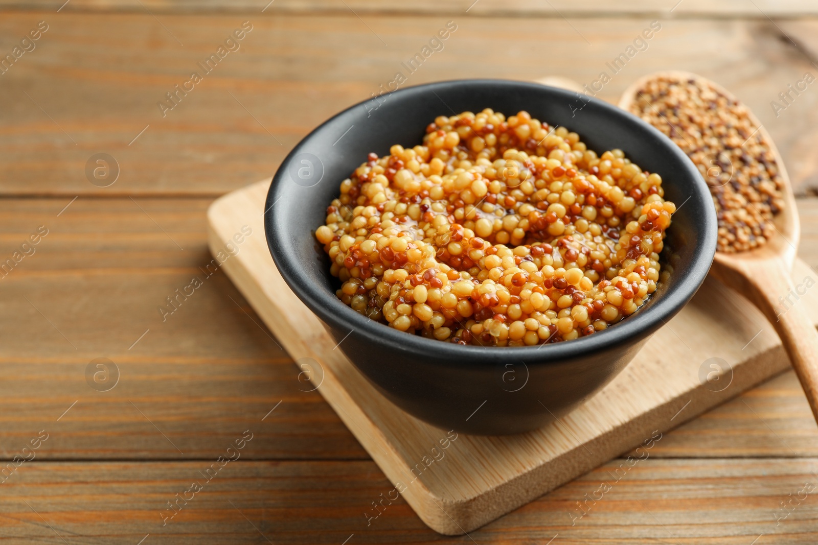 Photo of Fresh whole grain mustard in bowl on wooden table. Space for text