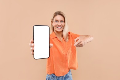 Photo of Happy woman holding smartphone and pointing at blank screen on beige background