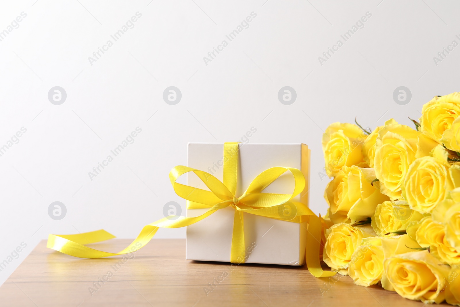 Photo of Beautiful bouquet of yellow roses and gift box on wooden table, space for text