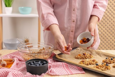 Photo of Making granola bars. Woman with dry fruits at table in kitchen, closeup