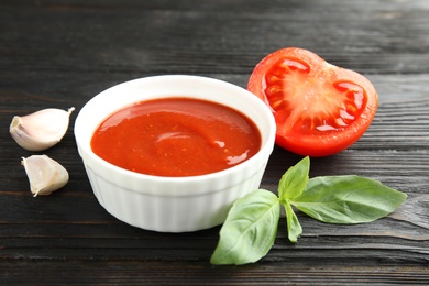 Composition with bowl of tomato sauce on wooden table, closeup