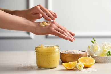 Photo of Woman applying body scrub on hand at wooden table, closeup