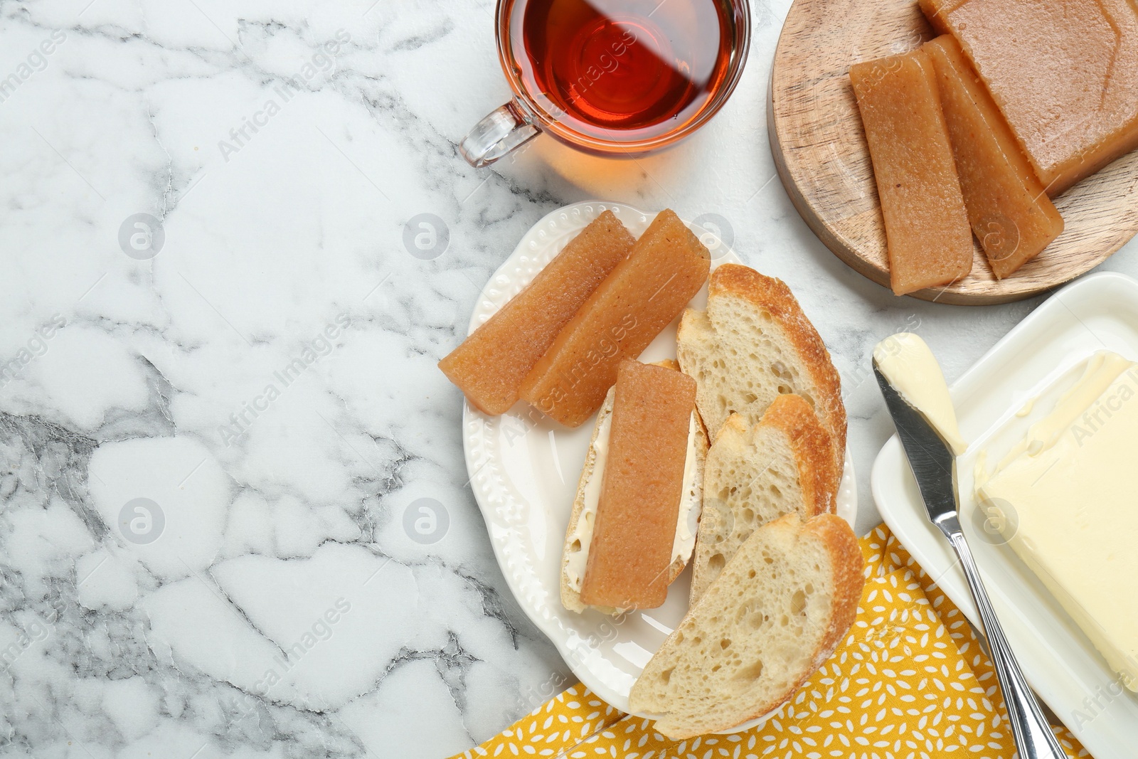 Photo of Delicious quince paste, bread, butter and cup of tea on white marble table, flat lay. Space for text