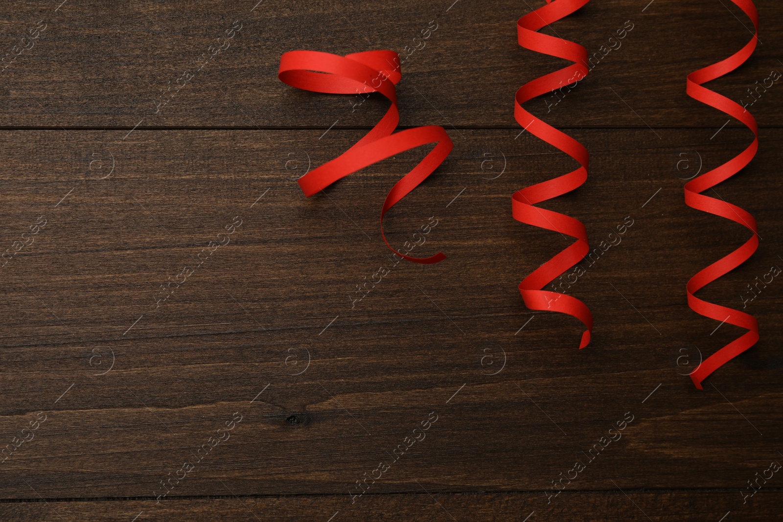 Photo of Red serpentine streamers on wooden table, flat lay. Space for text