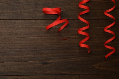 Photo of Red serpentine streamers on wooden table, flat lay. Space for text