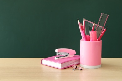 Photo of Different school stationery on wooden table near green chalkboard, space for text. Back to school