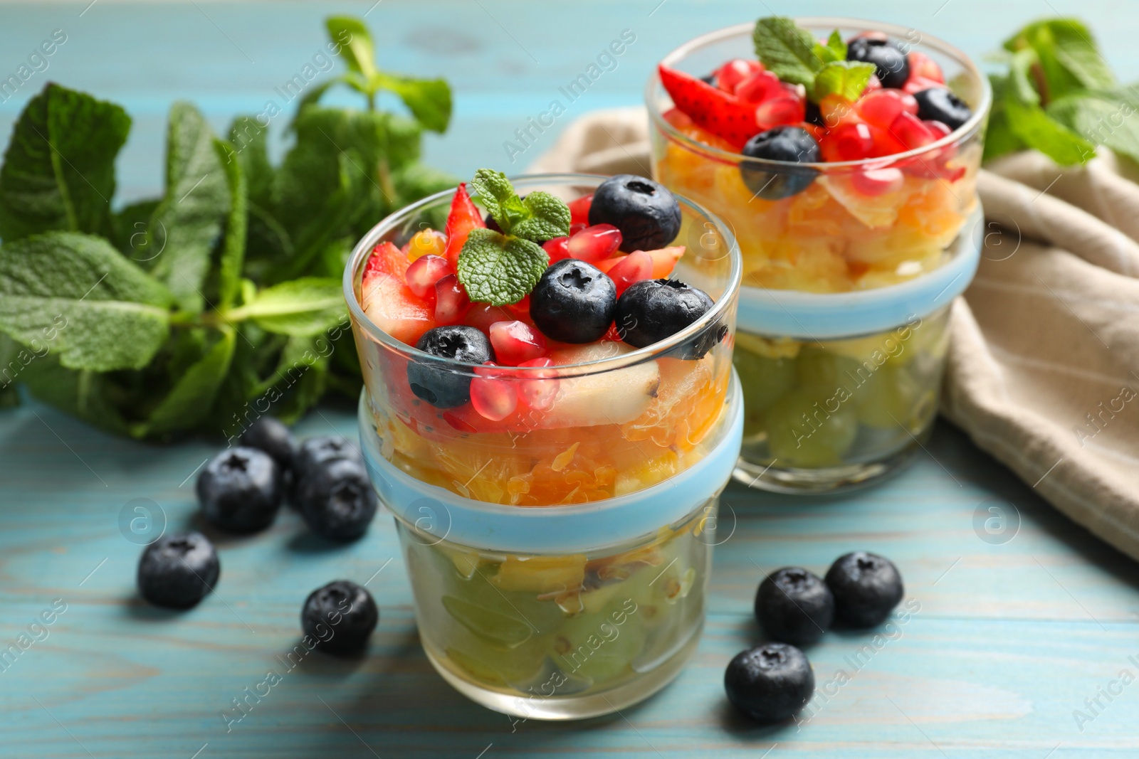 Photo of Delicious fruit salad in glasses, fresh berries and mint on light blue wooden table