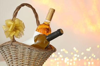 Photo of Wicker basket with bottles of wine against blurred lights, space for text