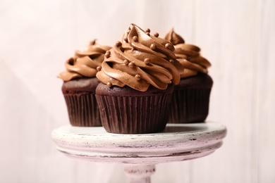 Photo of Delicious chocolate cupcakes with cream and beads on white stand, closeup