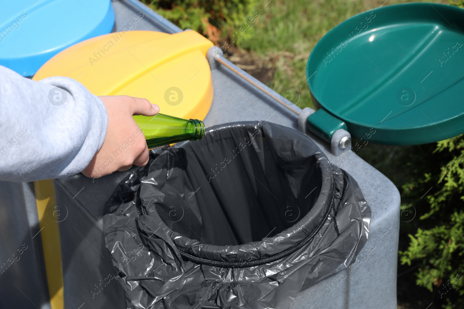 Photo of Woman throwing glass bottle in bin outdoors, closeup. Recycling concept