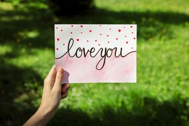 Photo of Woman holding card with phrase Love You outdoors, closeup