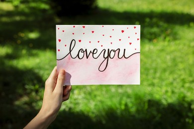 Woman holding card with phrase Love You outdoors, closeup