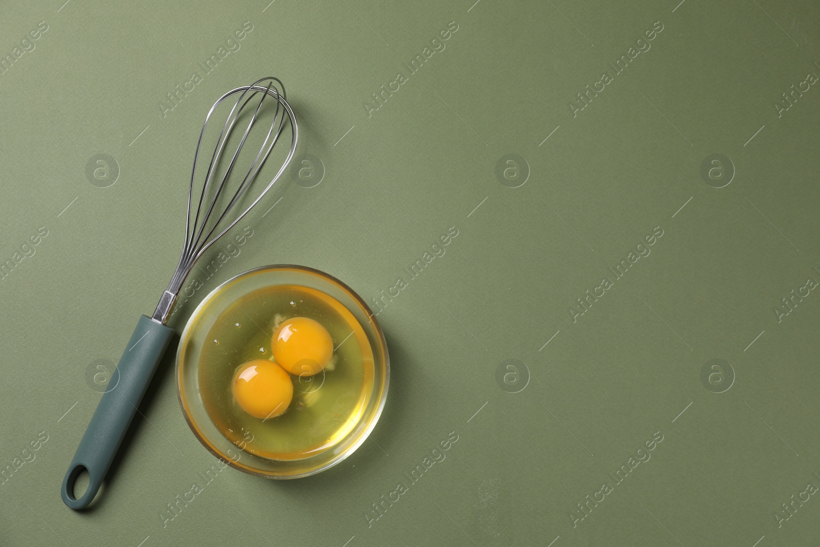 Photo of Metal whisk and raw eggs in bowl on khaki background, flat lay. Space for text