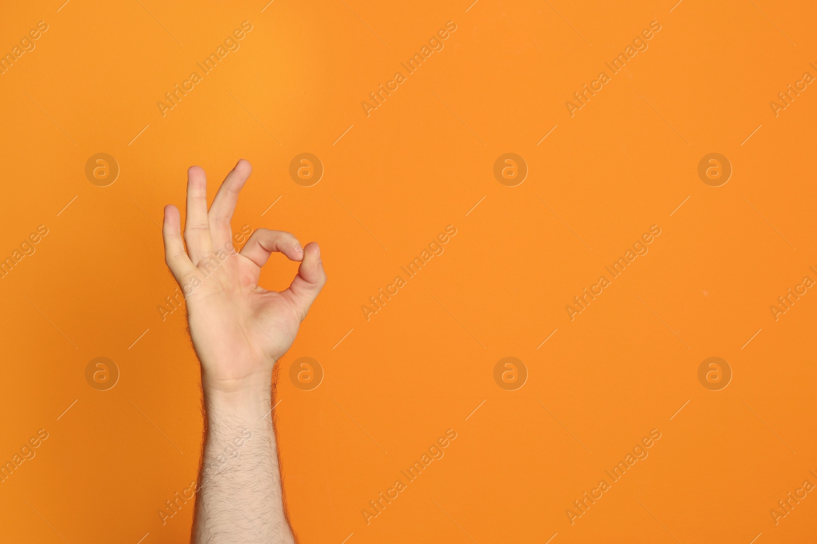 Photo of Young man showing OK gesture on color background. Space for text