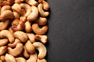 Photo of Tasty cashew nuts on black background, top view. Space for text