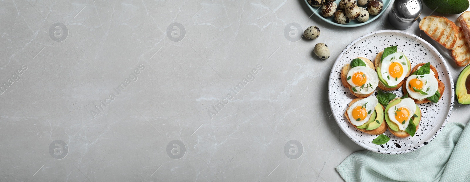 Image of Flat lay composition of tasty bruschettas with quail eggs and avocado on light grey marble table, space for text. Banner design 