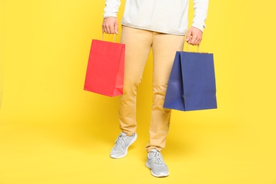 Photo of Young man with paper bags on yellow background, closeup