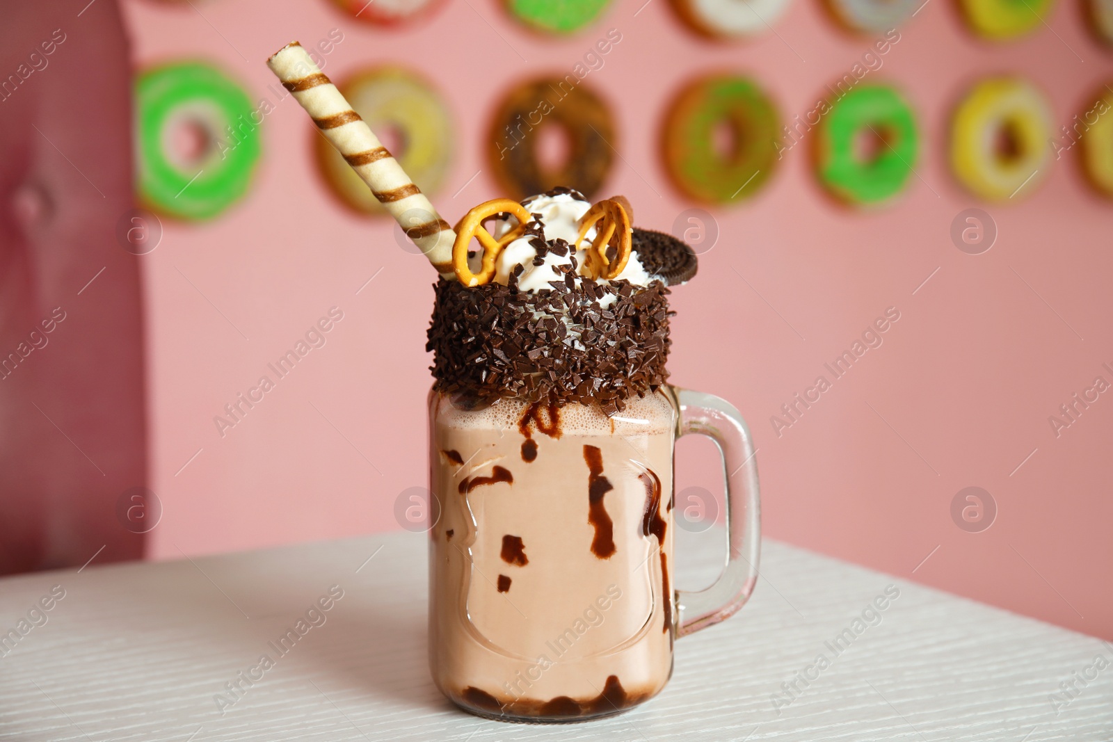 Photo of Tasty milk shake with sweets in mason jar on table at cafe