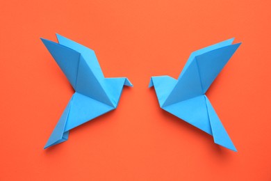 Photo of Beautiful light blue origami birds on orange background, flat lay