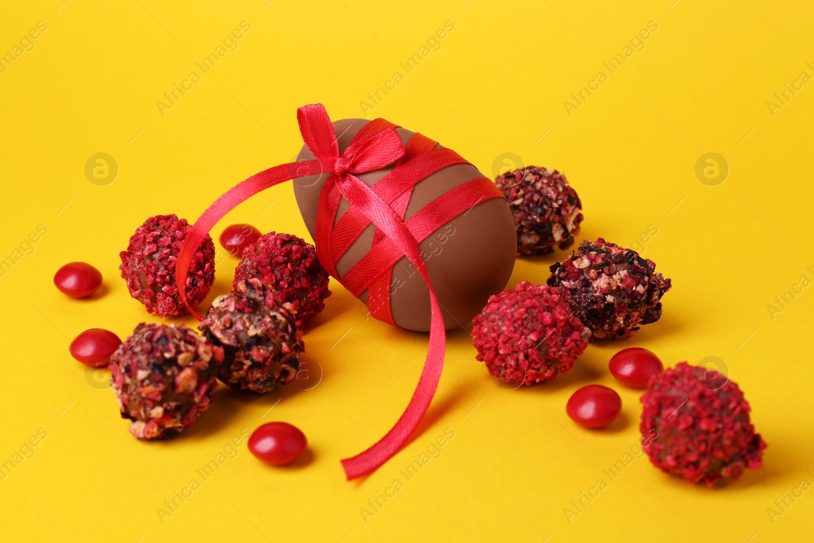 Photo of Tasty chocolate egg with red ribbon and candies on yellow background