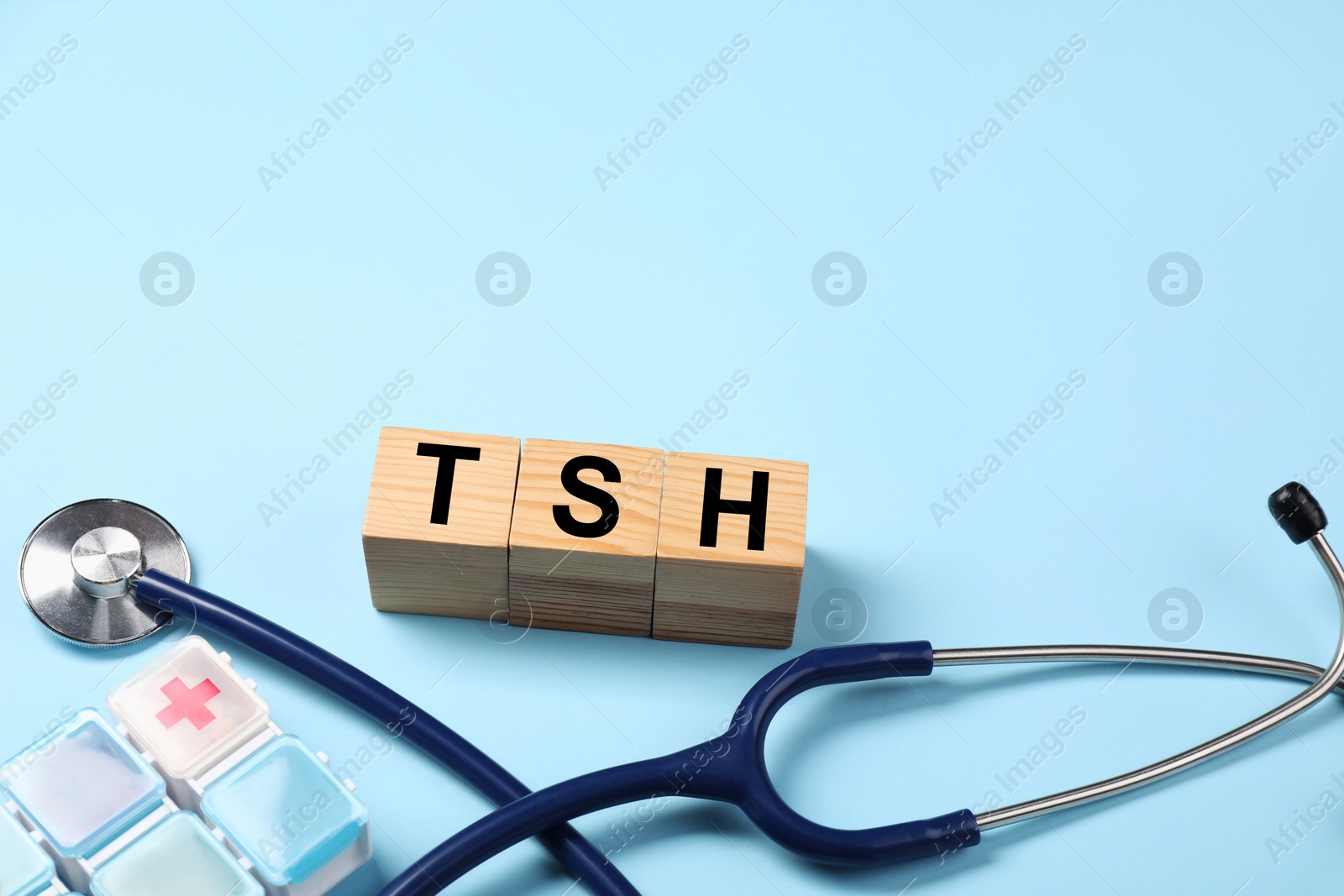 Photo of Endocrinology. Stethoscope, pills and wooden cubes with thyroid hormones on light blue background. Space for text