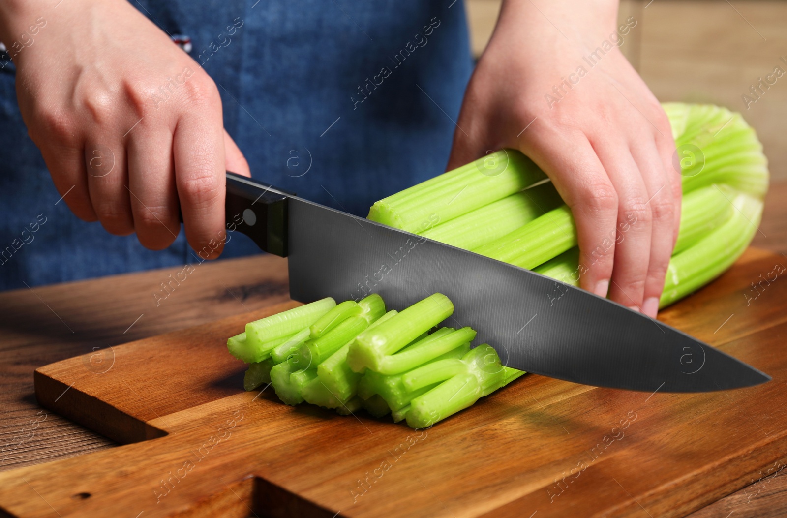 Photo of Woman cutting fresh green celery at wooden table, closeup