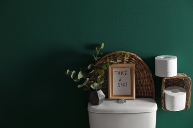 Decor elements, paper rolls and toilet bowl near green wall, space for text. Bathroom interior