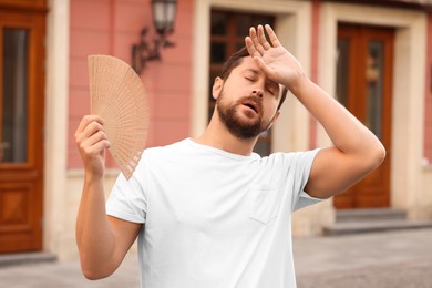 Man with hand fan suffering from heat outdoors