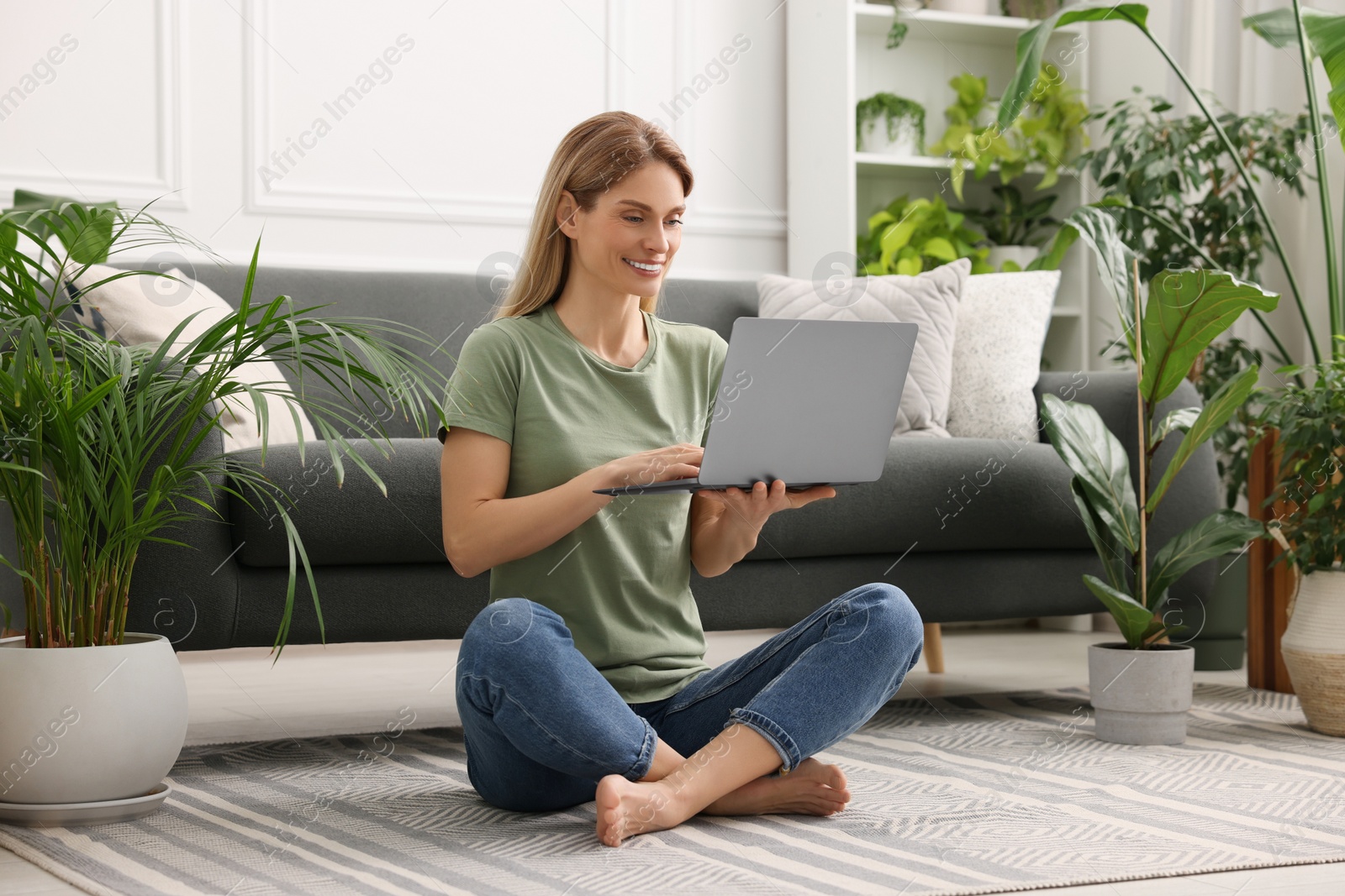 Photo of Woman using laptop surrounded by beautiful potted houseplants at home