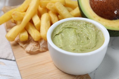 Photo of Serving board with french fries, guacamole dip and avocado on white wooden table, closeup
