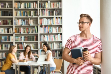 Photo of Young man with books and drink in library. Space for text