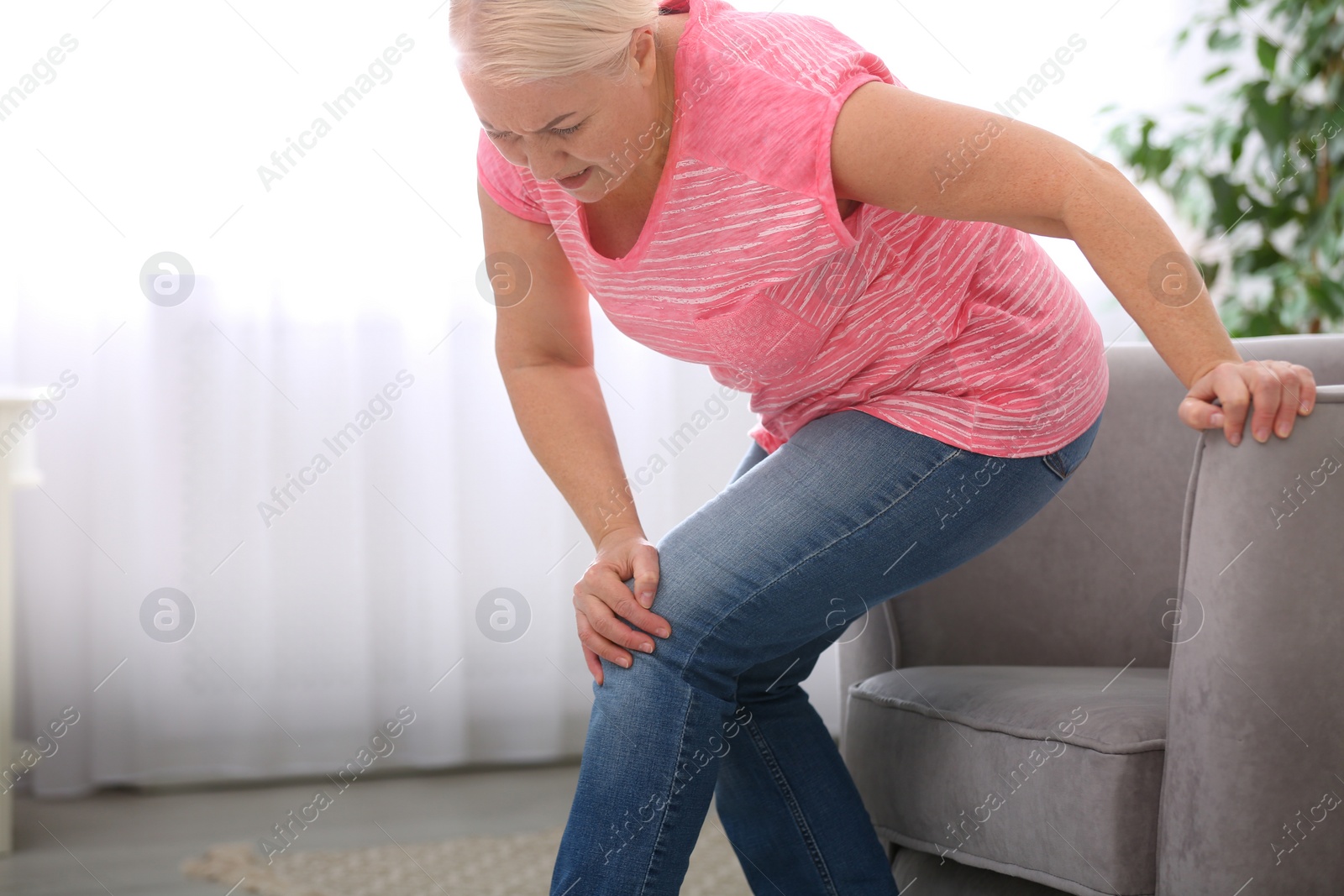 Photo of Senior woman suffering from knee pain in living room. Space for text