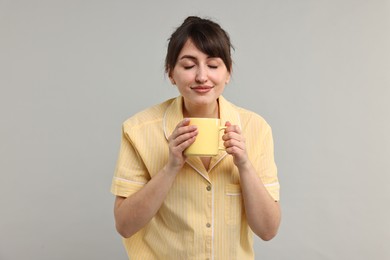 Photo of Woman in pyjama holding cup of drink on grey background