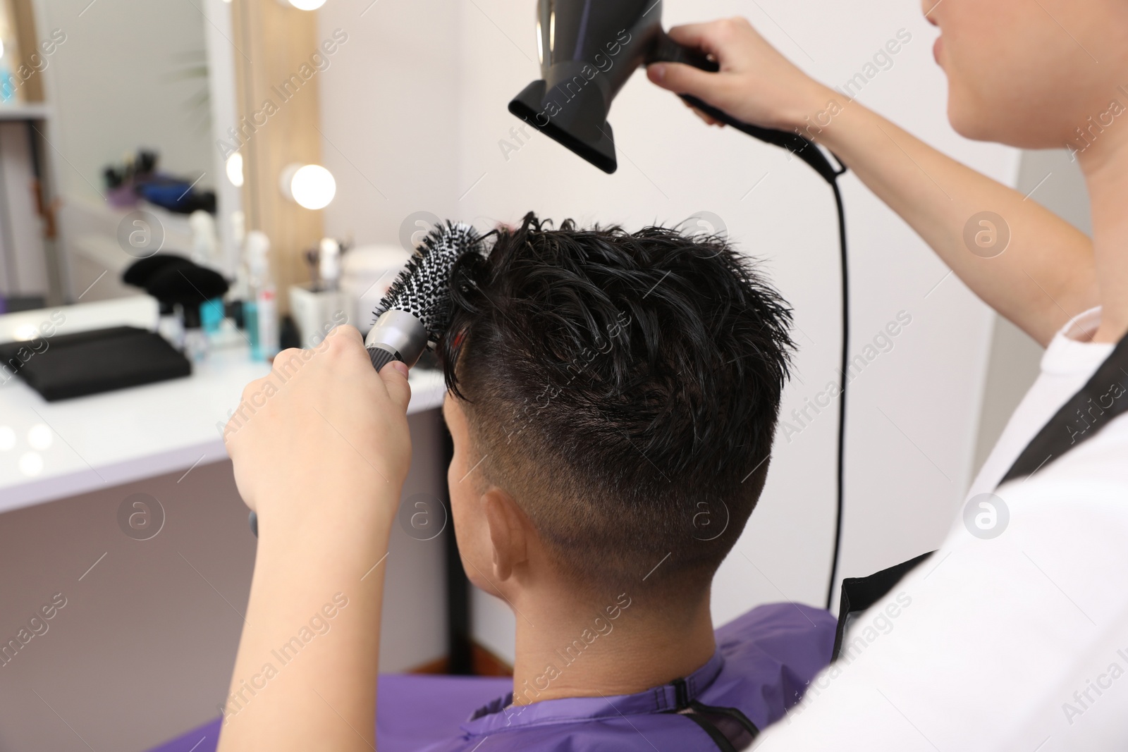 Photo of Professional hairdresser drying client's hair in salon, closeup