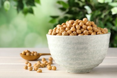 Photo of Raw chickpeas in bowl on white wooden table