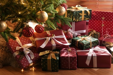 Photo of Pile of gift boxes near Christmas tree on floor