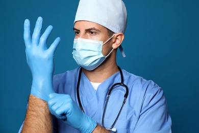 Photo of Doctor in protective mask putting on medical gloves against blue background