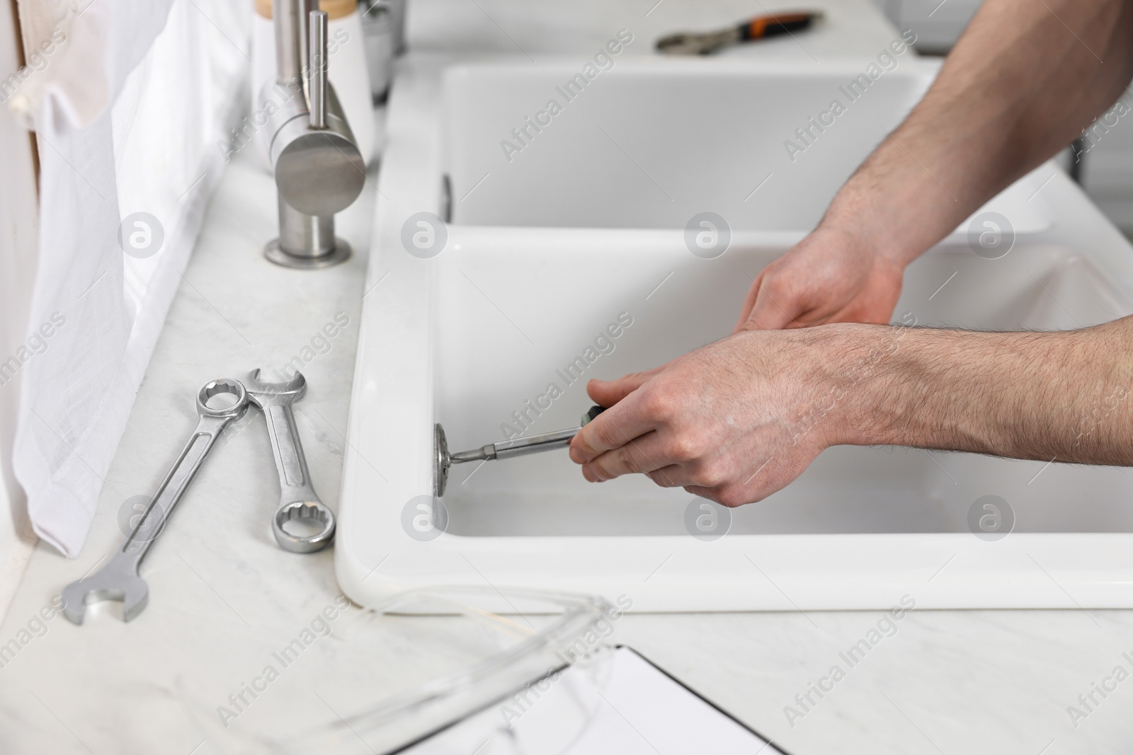 Photo of Plumber repairing sink with screwdriver indoors, closeup