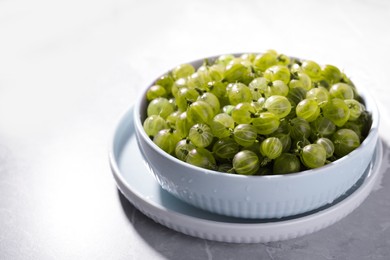 Photo of Bowl full of ripe gooseberries on light grey marble table, closeup. Space for text