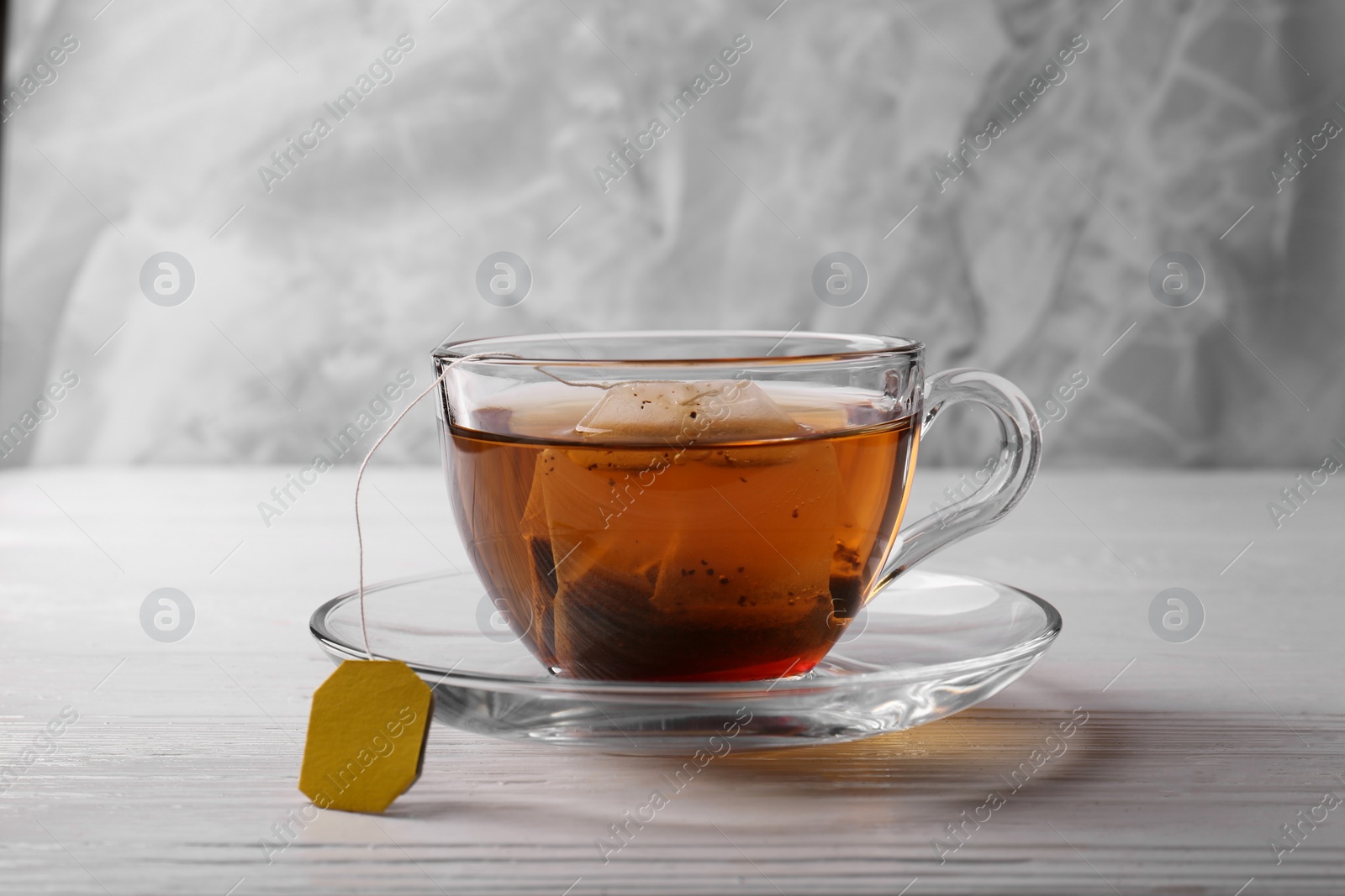 Photo of Tea bag in glass cup on white wooden table