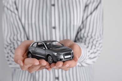 Photo of Insurance agent holding toy car on grey background, closeup