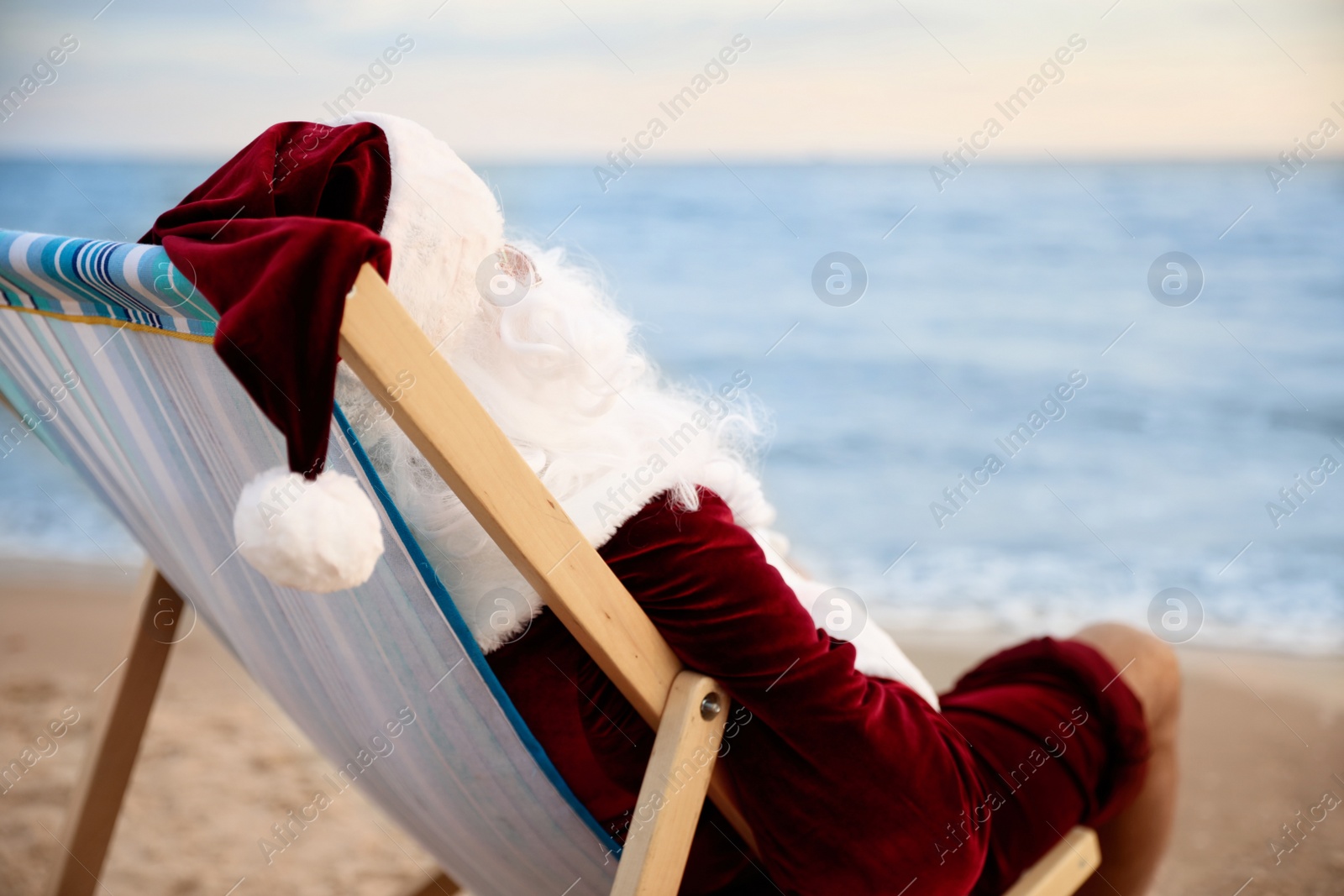 Photo of Santa Claus relaxing in chair on beach, space for text. Christmas vacation