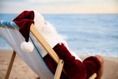 Photo of Santa Claus relaxing in chair on beach, space for text. Christmas vacation