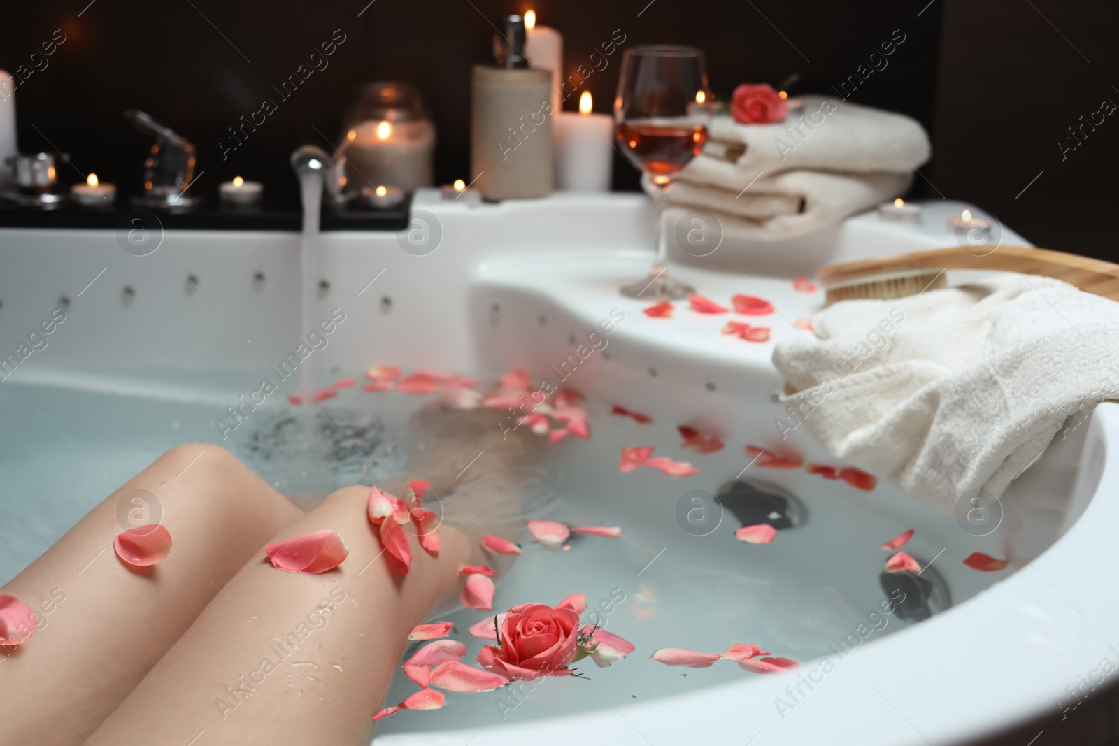 Photo of Woman taking bath with rose petals, closeup. Romantic atmosphere