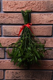 Photo of Mistletoe bunch with red bow hanging on brick wall. Traditional Christmas decor