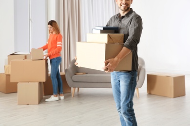 Man carrying moving boxes while woman unpacking other in new house